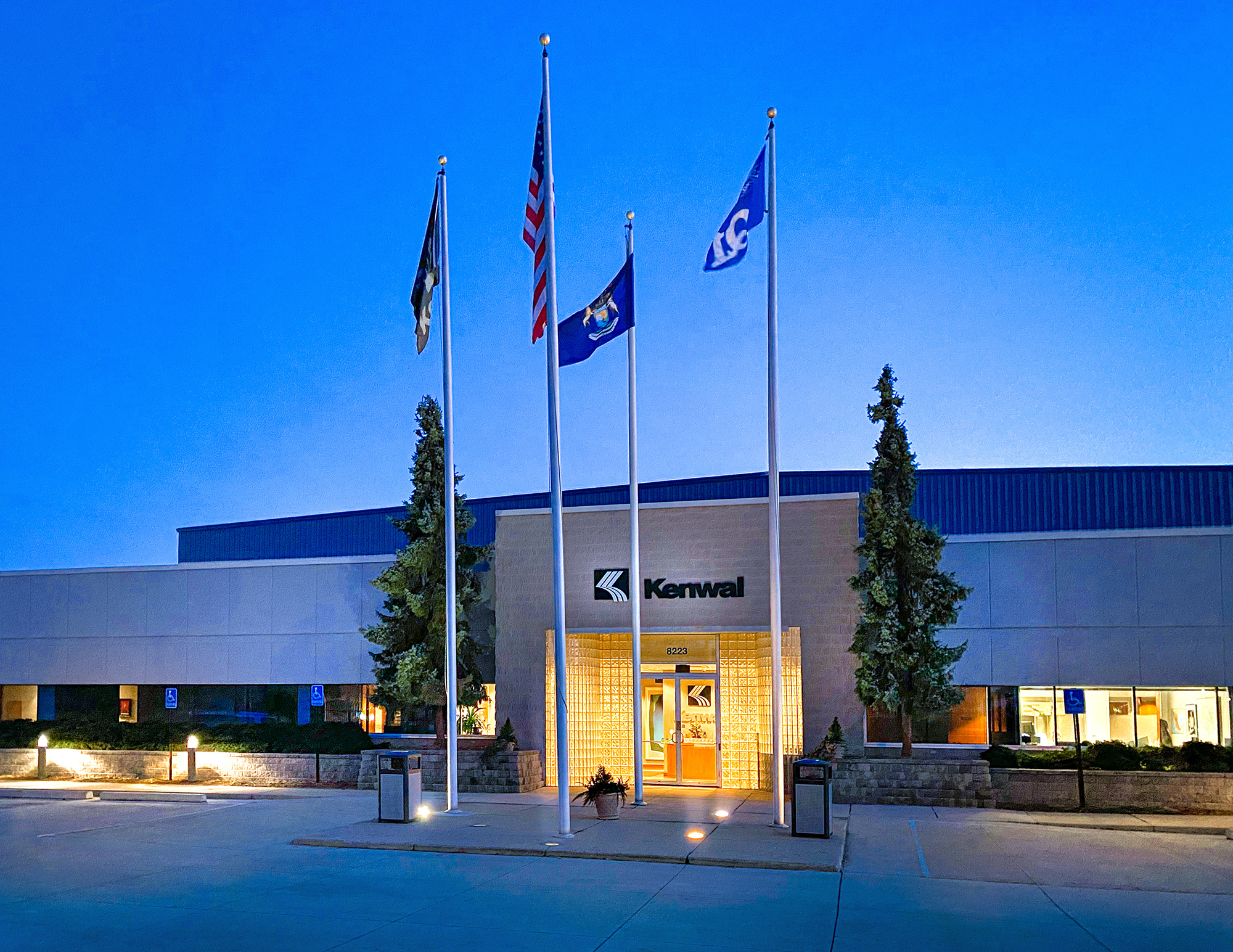 Kenwal_Dearborn Headquarters Kenwal's Dearborn headquarter's building, interior lights on and 4 flags standing in front of entrance