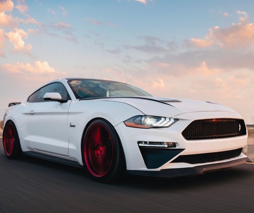 Industries – Automotive Close-up side view of a sleek white sports car with red custom wheels driving on highway at sunset.