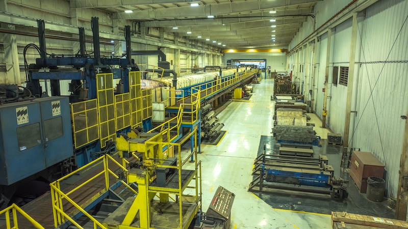 default View of an industrial steel coil processing line inside Kenwal Steel’s manufacturing plant, featuring machinery, conveyor systems, and yellow safety railings.