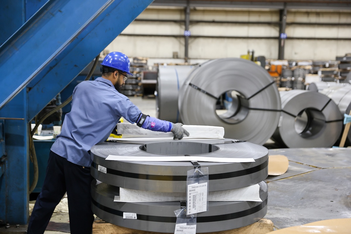 Steel coil processing at a manufacturing facility Forklift operator transporting stacked steel coils inside a large industrial warehouse.