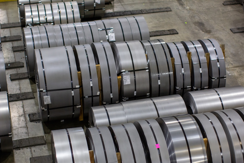 Rolled steel coils stored in an industrial warehouse, stacked on wooden supports and ready for processing or distribution.