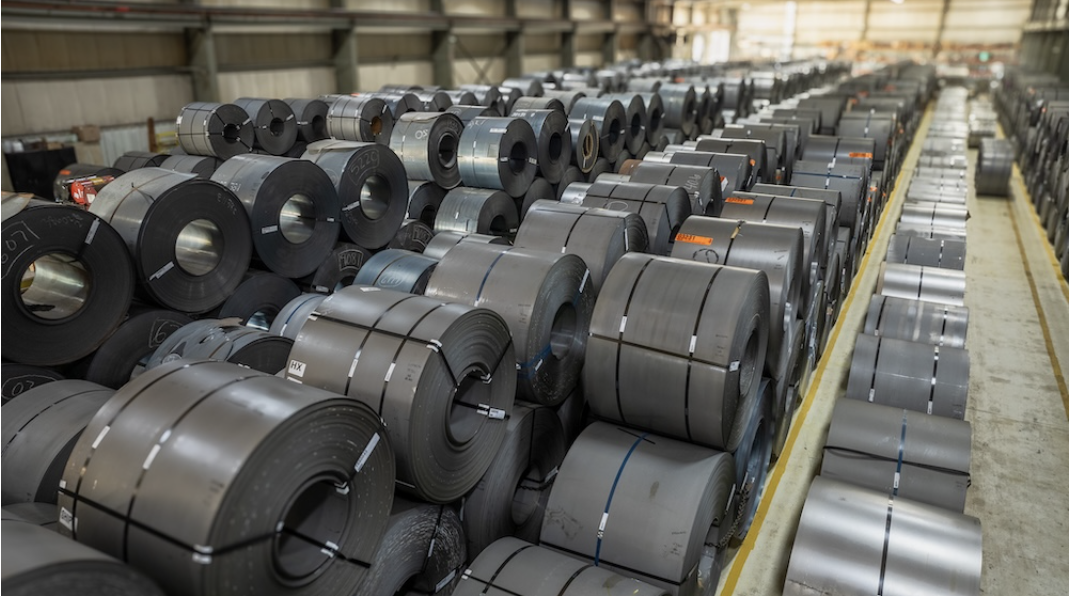 steel coil inventory warehouse Large warehouse filled with neatly stacked coils of rolled steel, organized in rows for industrial storage and distribution.