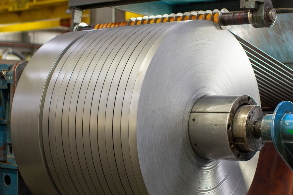 steel-coil-slitting-machine-process Close-up of a steel coil being slit into narrow strips by an industrial slitting machine in a metal processing facility.