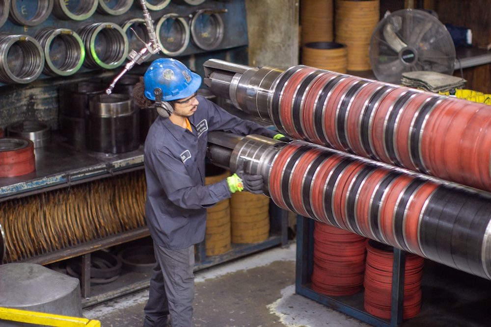 steelworker-adjusting-slitter-tooling Steelworker adjusting slitter tooling on a metal processing line, surrounded by industrial equipment and safety gear.
