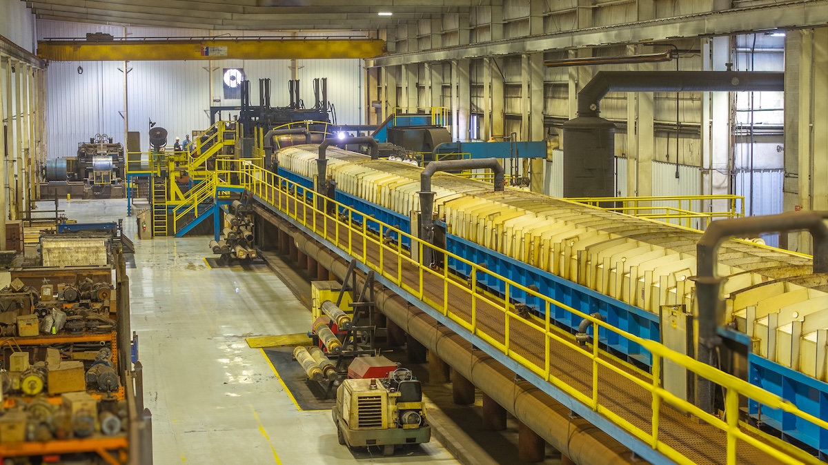 default Interior view of a steel service center with stacked steel coils, overhead cranes, and workers operating machinery under high-bay lighting.