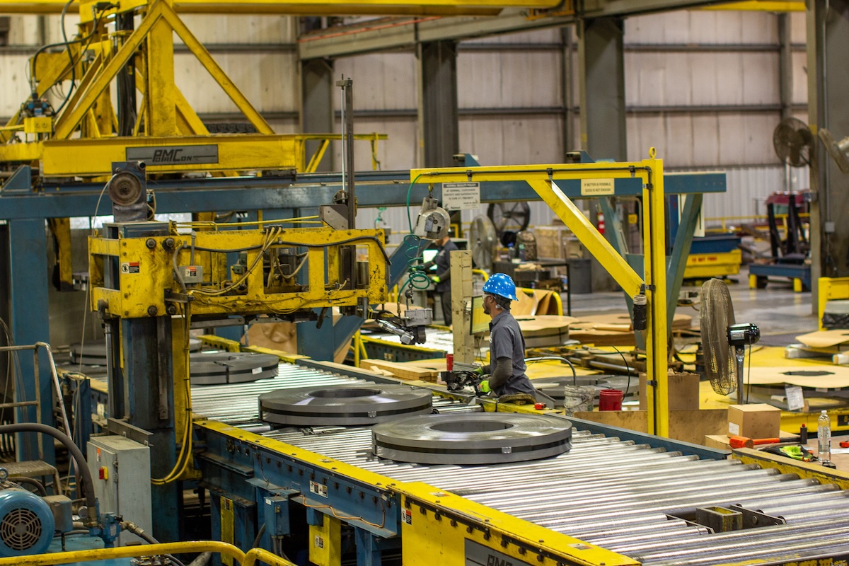 Steel packaging (1) Smiling forklift operator posing with raised arms inside a steel processing facility, showcasing employee pride and workplace positivity.