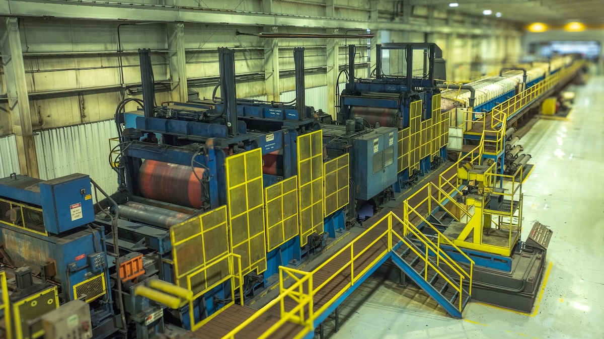 default Industrial tension leveling and pickling line inside a steel processing plant, featuring large blue machinery, yellow safety railings, and metal rollers used for flattening and surface treatment of steel coils.