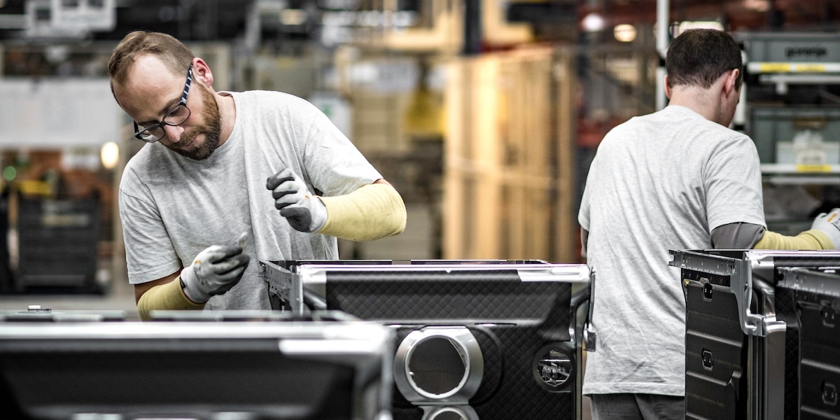 Workers assembling metal components in manufacturing facility Two factory workers wearing safety gloves assembling metal components on a production line inside an industrial manufacturing facility.