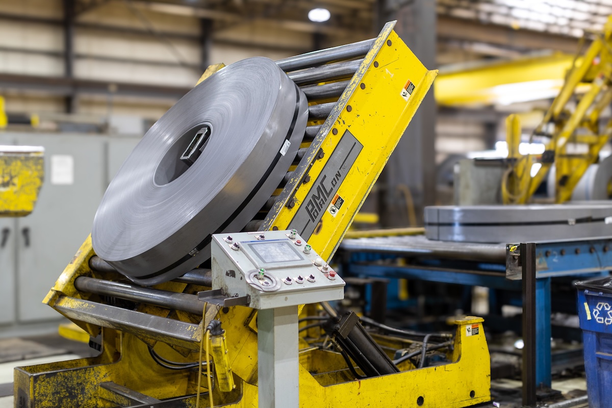 steel packaaging proccess Steel coil being unrolled and fed into a leveling or cutting machine at a metal processing facility.